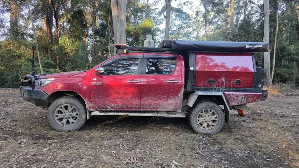 Mud-splashed red Hilux tray-back parked in the bush